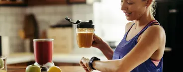 mulher olha para o relógio e segura numa taça com batido