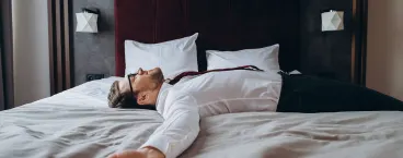 homem na cama de hotel com sintomas de jet lag