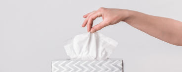 mulher a retirar lenço de papel de uma caixa de lenços