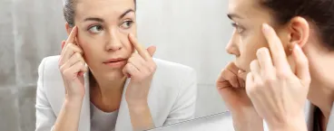 mulher a verificar as suas olheiras ao espelho