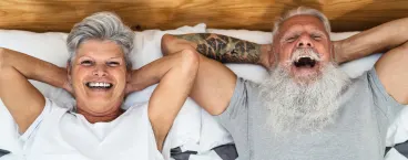 casal de séniores deitados na cama a sorrirem