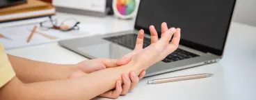 mulher em frente ao computador a massajar a mão