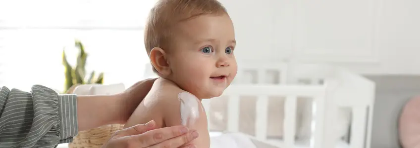 mãe a colocar creme nos ombros do bebé