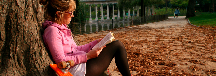 Mulher a ler um livro encostada a uma árvore