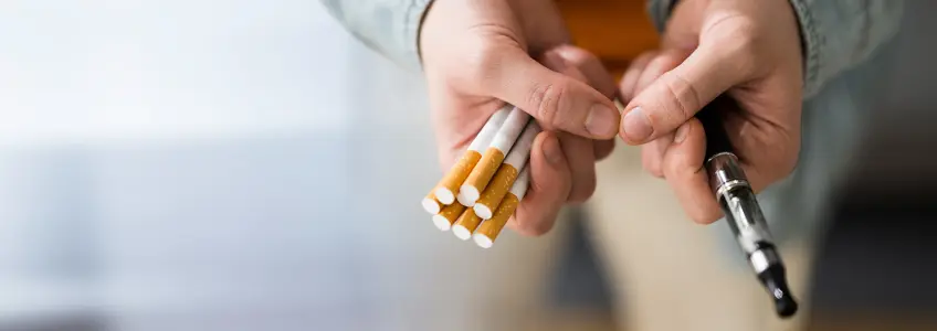 homem com cigarros tradicionais numa mão e um cigarro eletrónico na outra