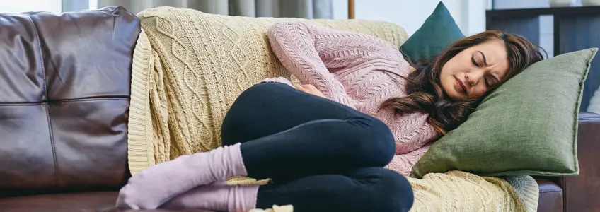 mulher com botija de água quente na barriga, sentada no sofá