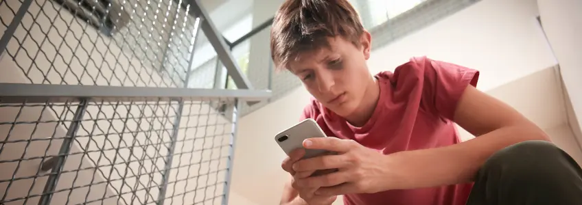 rapaz jovem com olho magoado a mexer no telemóvel