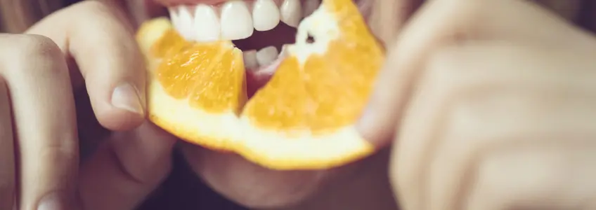 mulher a trincar fatia de laranja