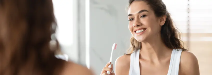 mulher jovem em frente ao espelho com escova de dentes
