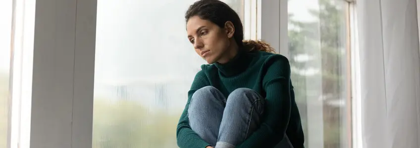 mulher com ar triste encostada a uma janela