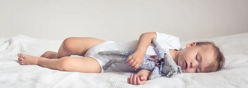 bebé a dormir agarrado a um boneco