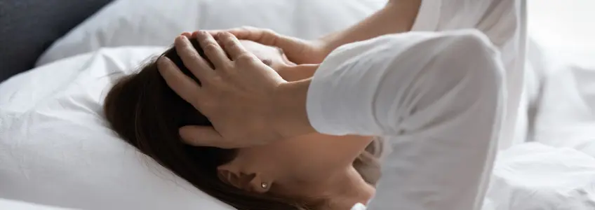 mulher deitada na cama com as mãos na cabeça