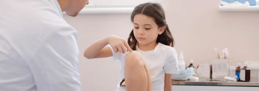 menina indica ao médico onde costuma sentir dor nas pernas