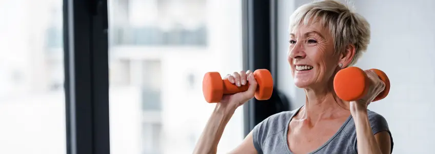 senhora sénior a levantar dois halteres de ginástica