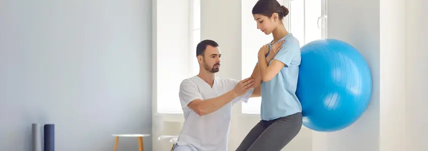 rapariga a fazer exercício com bola suíça e ajuda de fisioterapeuta