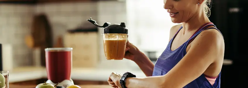 mulher olha para o relógio e segura numa taça com batido
