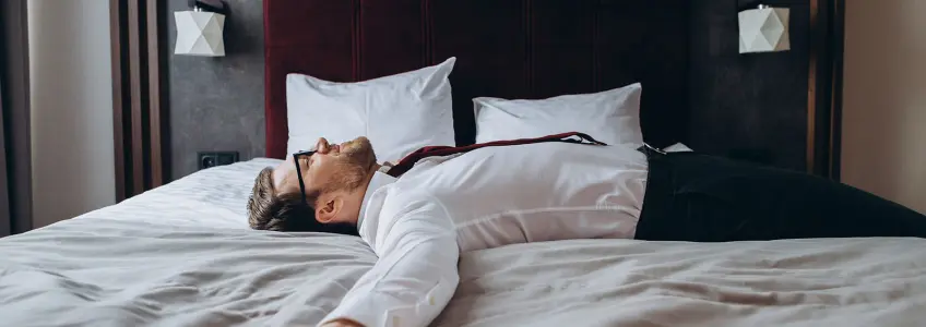 homem na cama de hotel com sintomas de jet lag