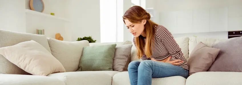 mulher jovem encolhida no sofá com cólicas