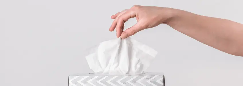 mulher a retirar lenço de papel de uma caixa de lenços