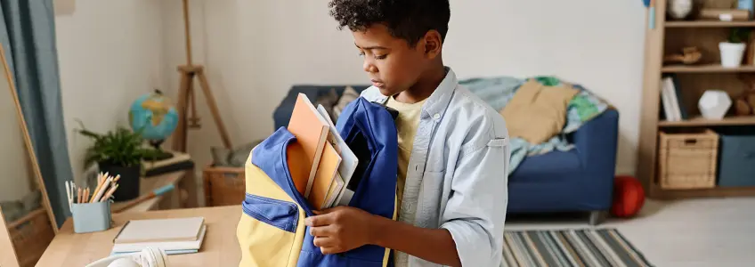 menino a colocar livros na mochila da escola
