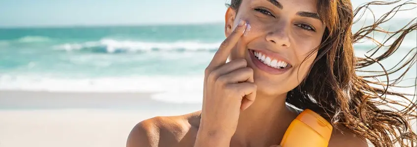 mulher sorridente na praia a aplicar protetor solar