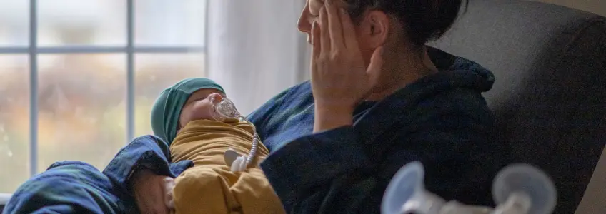 mãe com dores de cabeça a segurar o seu recém nascido