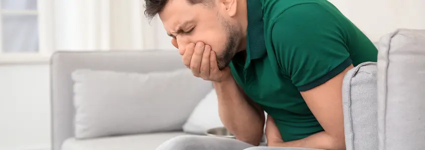 homem sentado no sofá com dores abdominais