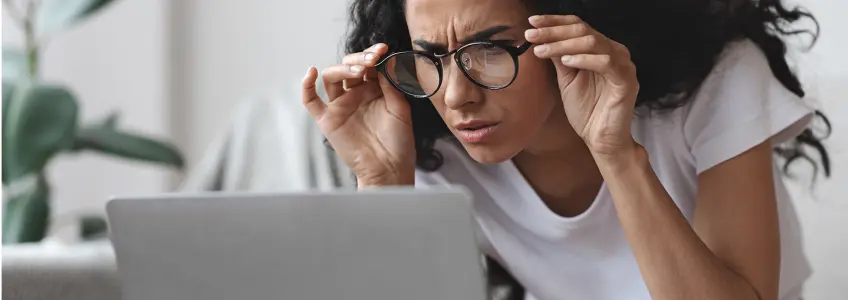 mulher com dificuldade em focar o que está no ecrã do computador