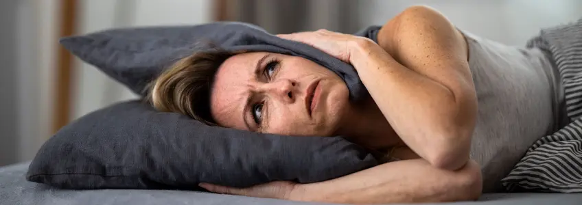 senhora deitada na cama a tapar os ouvidos com uma almofada